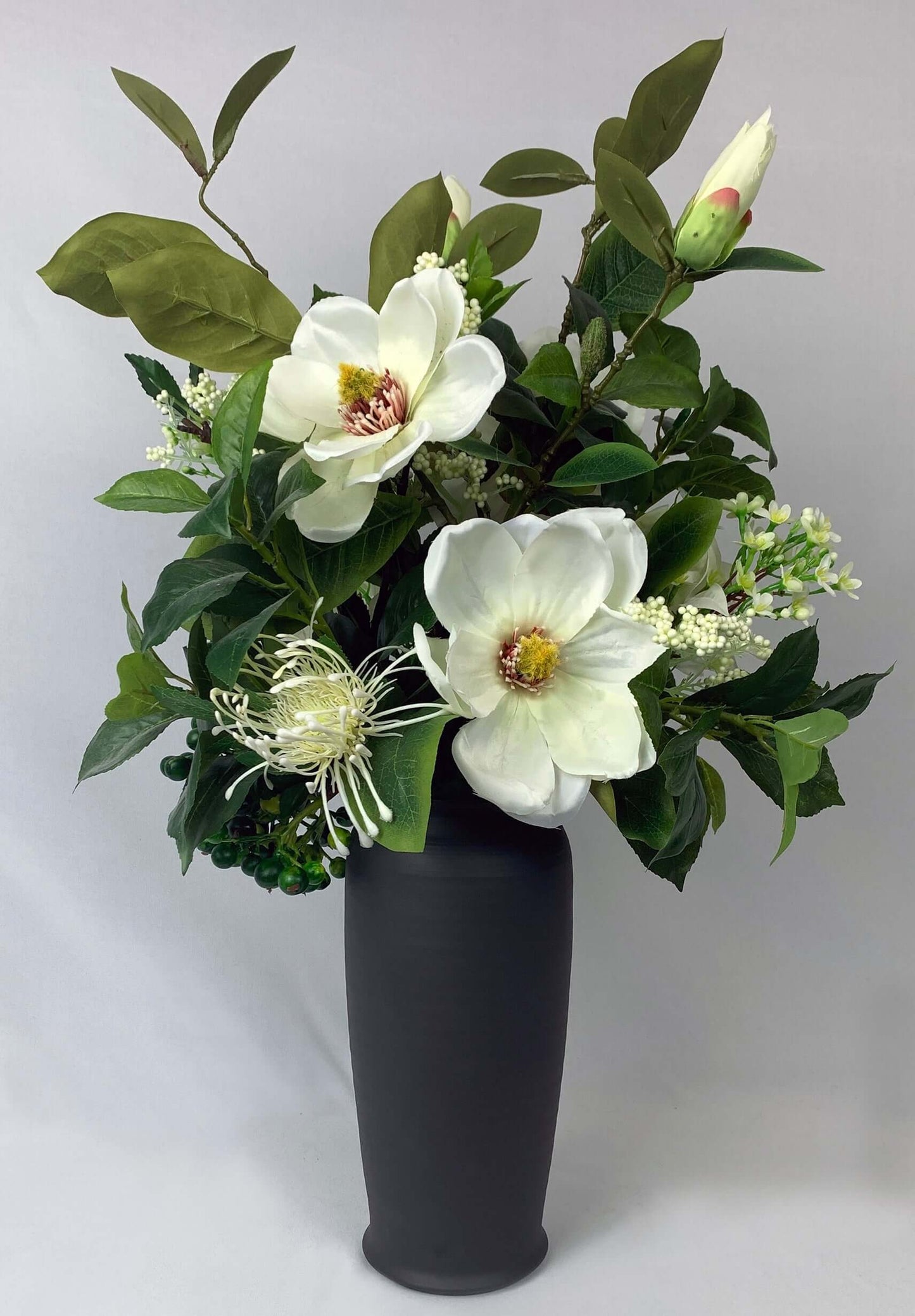 Magnolias, bougainvillaea, wax flower, spider chrysanthemums and green berries in a tall black ceramic vase, inspired by "Old South" romance.  Size:  W34xH58cm  *Found Object – may not mean a new vessel/vase, but one which has been ‘found’ during our searches.