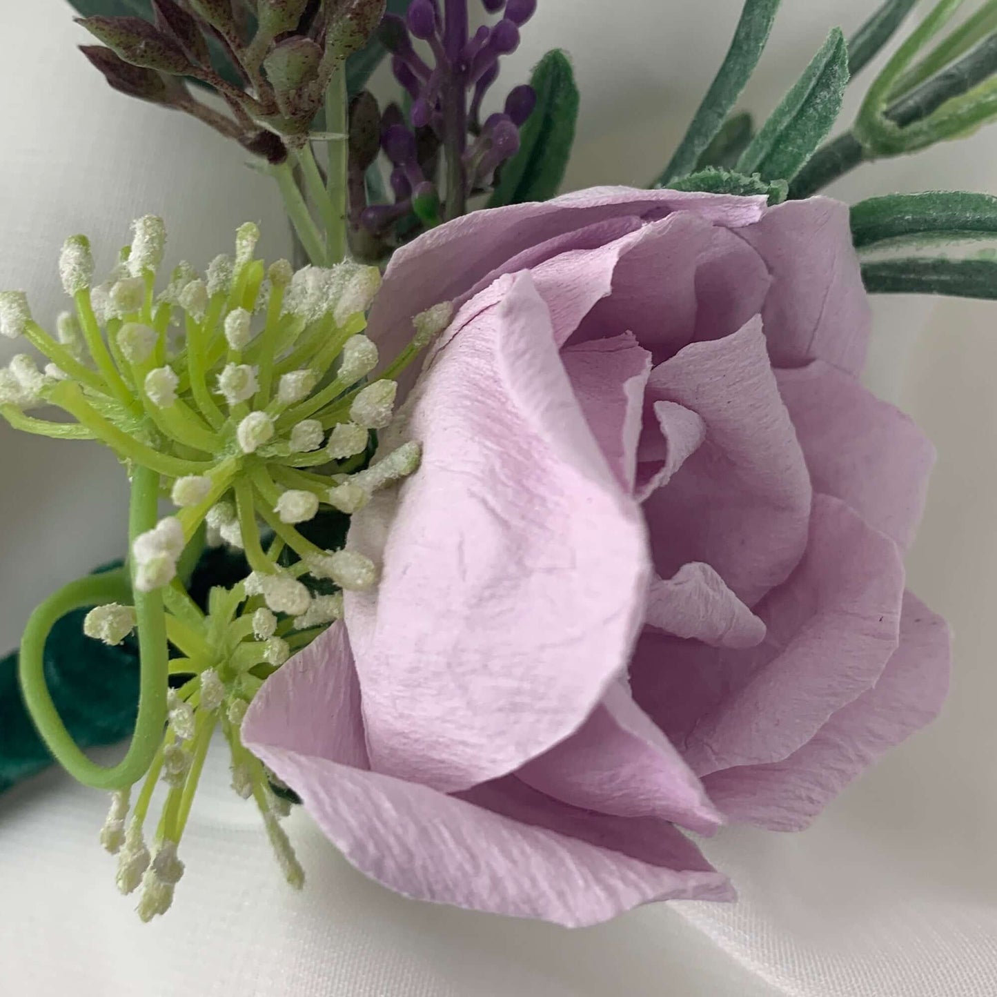 A beautiful hand-crafted paper (faux) large lilac rose boutonnieres, with a green satin stem, mixed with artificial flowers and foliage, are made to order to match your wedding theme colour and are perfect for the groom, the groomsmen, and fathers for your special occasion. Atelier Blooms