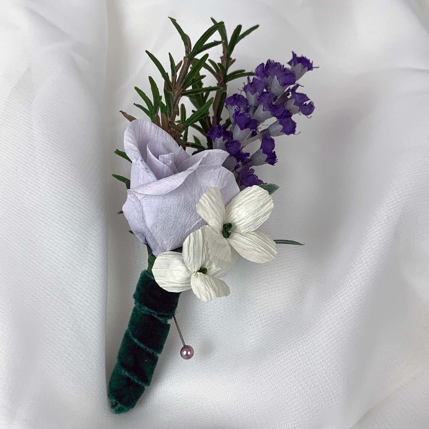 A beautiful hand-crafted paper (faux) small mauve rose boutonnieres, with a green satin stem, mixed with artificial flowers and foliage, are made to order to match your wedding theme colour and are perfect for the groom, the groomsmen, and fathers for your special occasion. Atelier Blooms