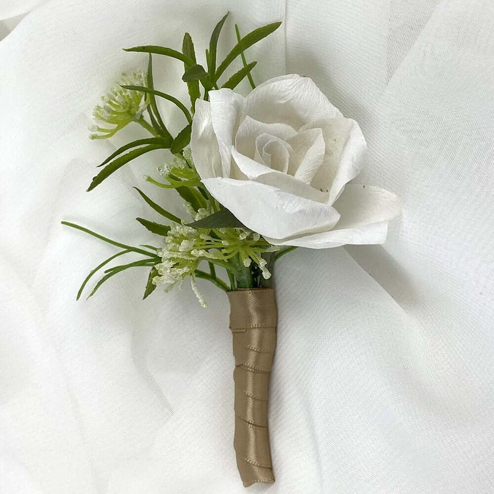 A beautiful hand-crafted paper (faux) white rose boutonnieres with a brown satin stem, mixed with artificial foliage, are made to order to match your wedding theme colour and are perfect for the groom, groomsmen, and fathers for your special day. Atelier