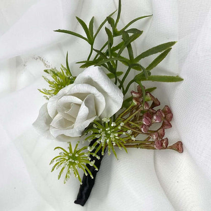 A beautiful hand-crafted paper (faux) white rose boutonnieres with a balck satin stem, mixed with artificial foliage, are made to order to match your wedding theme colour and are perfect for the groom, groomsmen, and fathers for your special day. Atelier Blooms