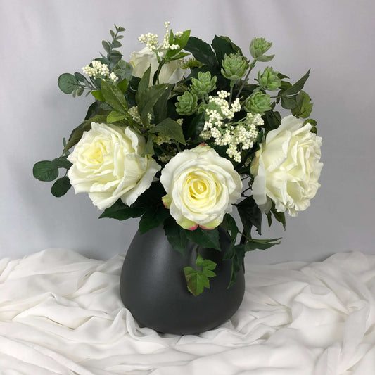 Beautiful arrangement of ivory peonies and roses mixed with green foliage in a large black jug.  Size: H47xW40cm  *Found Object – may not mean a new vessel/vase, but one which has been ‘found’ during our searches.