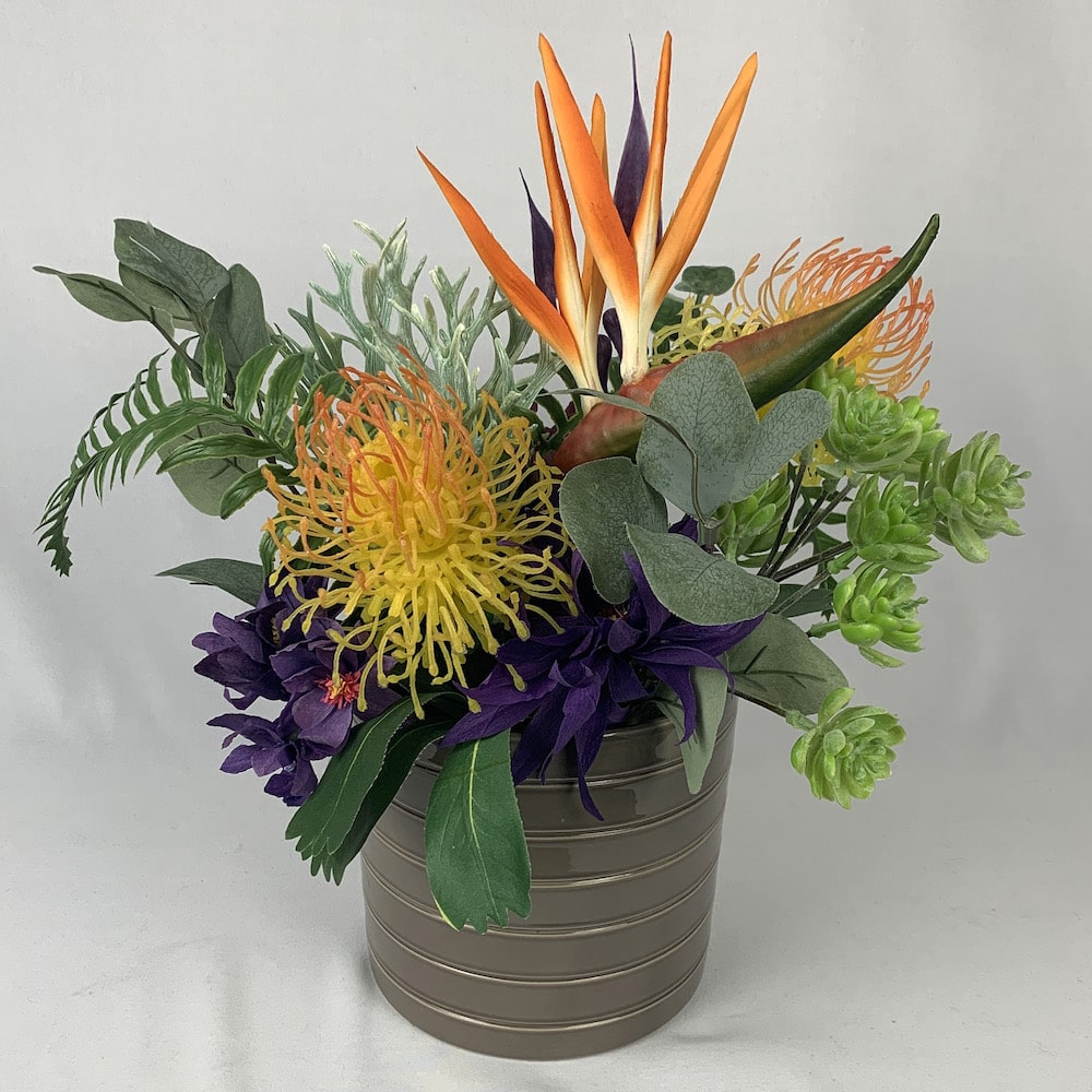 Tropical delights of Bird of Paradise, protea, and succulent touches, gathered together in a taupe coloured ceramic vase*. This stunning artificial flower arrangement will definitely brighten a corner of your room or a bookcase.  Size: W35 x H35cm   *Found Object – may not mean a new vessel/vase, but one which has been ‘found’ during our searches.  Please note: Sale price is for pictured item (Floor model) - ONE ONLY.